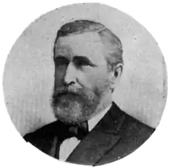 A black and white circular portrait of a Caucasian man in a suit and bow tie