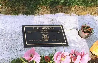 A bronze plaque headstone set in a block of concrete amongst grass, with flowers in the foreground.