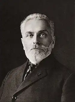 A photograph of a man in late middle age, with a short, neatly-trimmed beard, wearing formal dress.