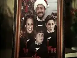 A framed Christmas family portrait. The father, mother, and two sons are wearing identical sweaters.