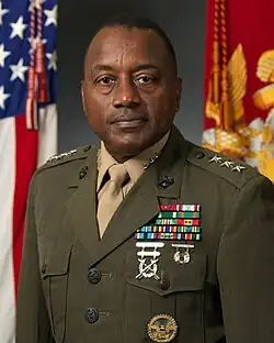 An African-American male dressed in Marine Corps olive green and khaki service uniform; his shoulder epaulettes have 3-stars; his left chest has many military ribbons and medals.
