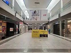 Interior hallway, 2024, with Uniqlo, Zara, and Bloomingdale's. An advertisement for H&M and Weichert, Realtors is central.