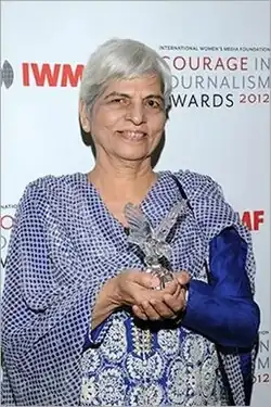 Silver-haired lady wearing a blue and white shawl holding a glass trophy; against the backdrop of IWMF logo