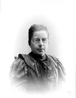 A vintage black-and-white portrait of a middle-aged woman. She is dressed in elegant early 20th-century attire. Her dark hair is neatly styled, and she has a calm, composed expression.