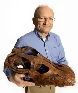 The photograph shows Hans-Dieter Sues holding a cast of a reconstructed skull of Brontosaurus at the Smithsonian.